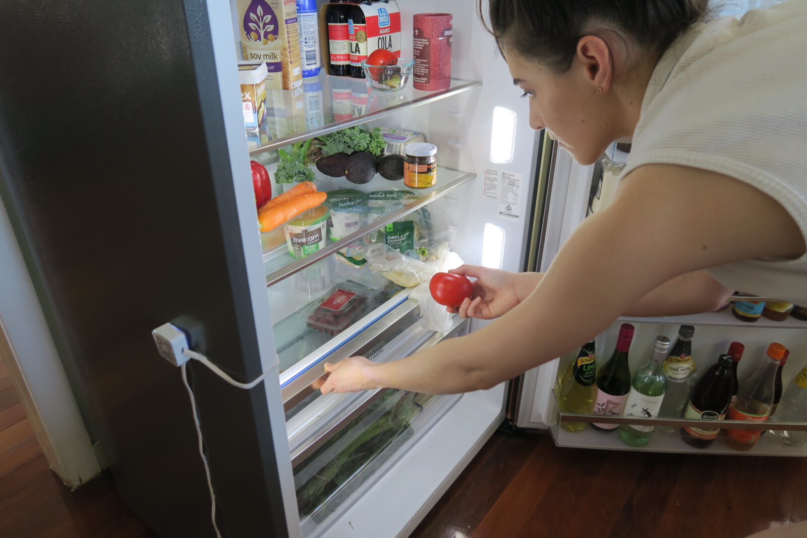In context model photograph of user filling fridge with fresh food. 
